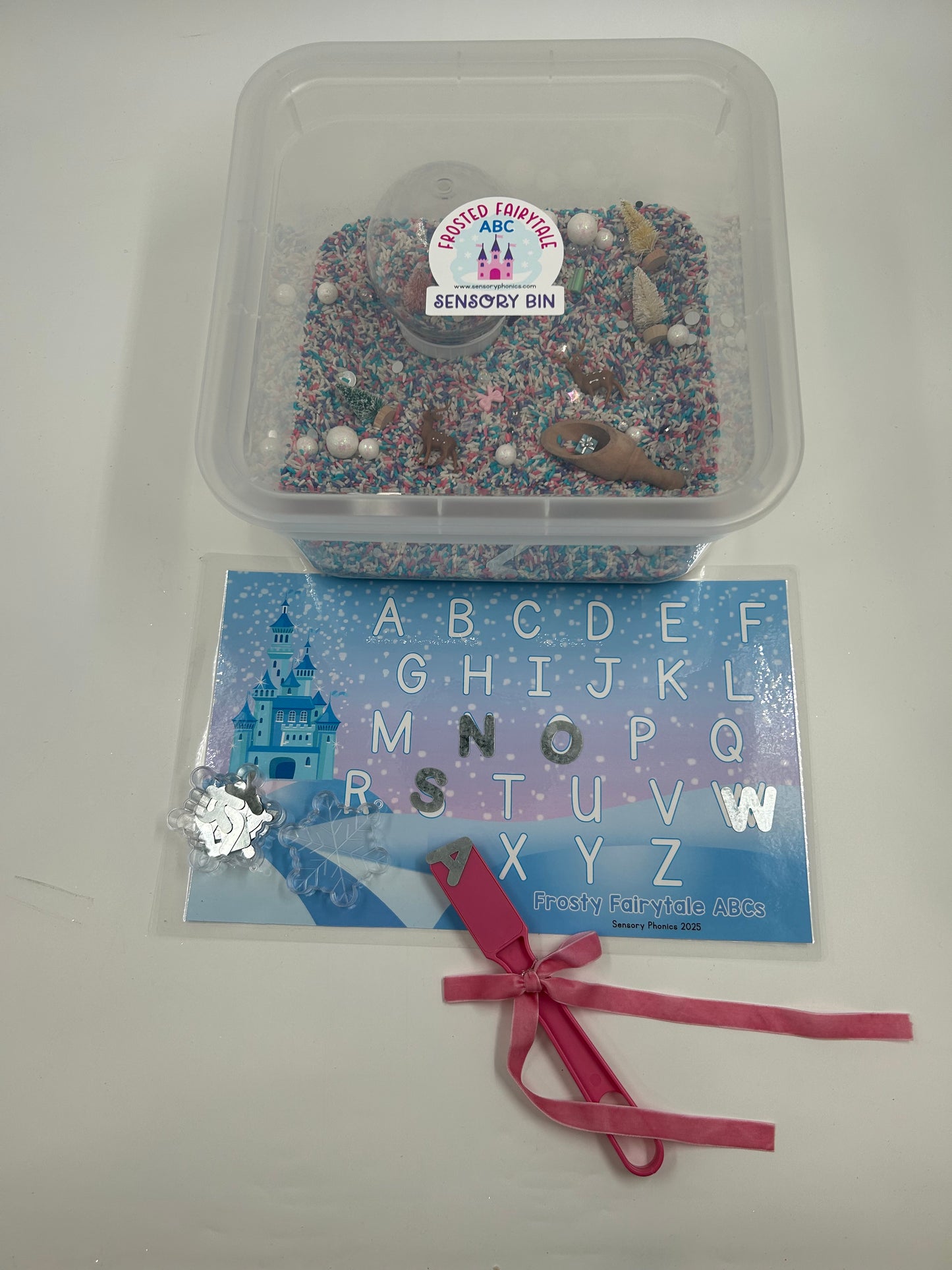 Clear container with pastel sensory rice including a pink magnetic wand with a pink bow, metal uppercase letters and a laminated letter matching mat, on a white background.