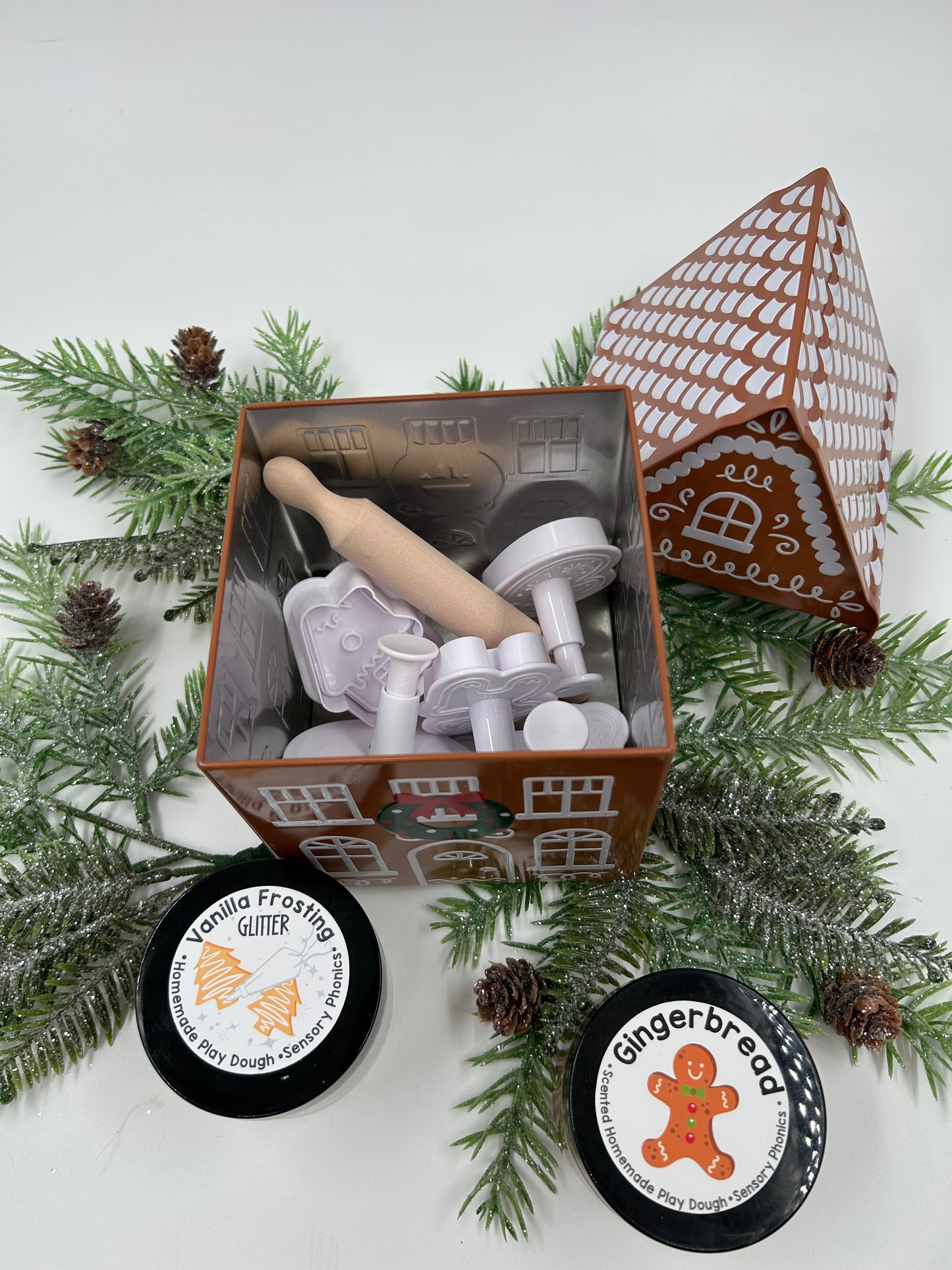 Set of gingerbread-themed play dough, cookie cutters and rolling pin with packaging on a decorative background.