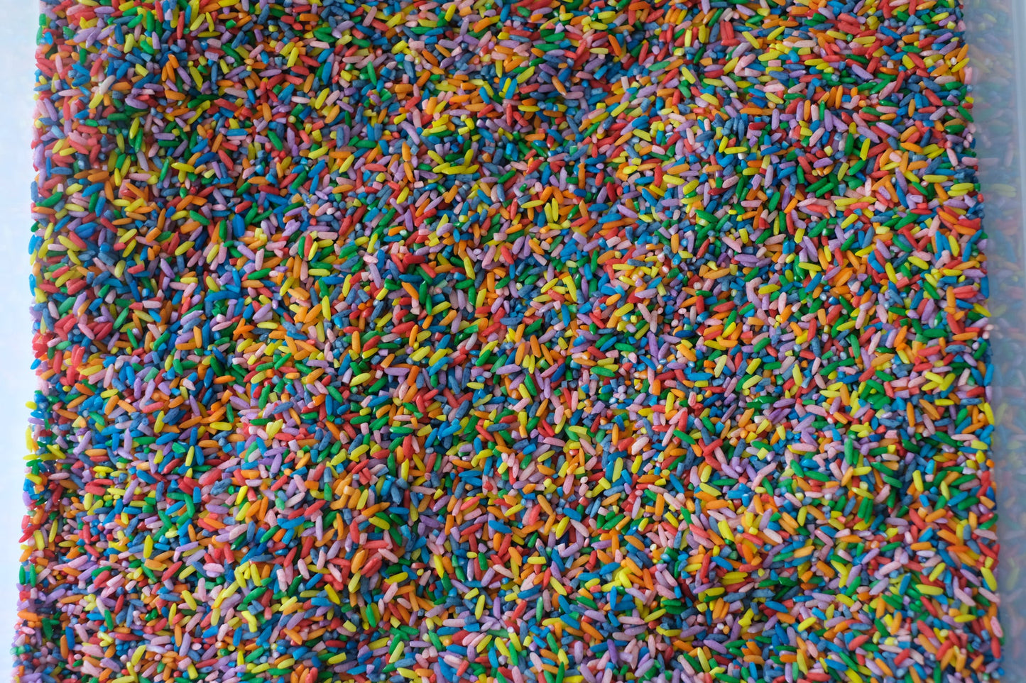 Colorful grains of dyed rice mixed together. Rainbow rice shown in clear container to show product in use.